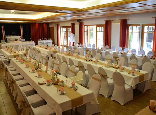 Liebevoll eingerichteter Festsaal mit großen Tischtafeln und schönen weißen Hussen, sowie einer Bühne.