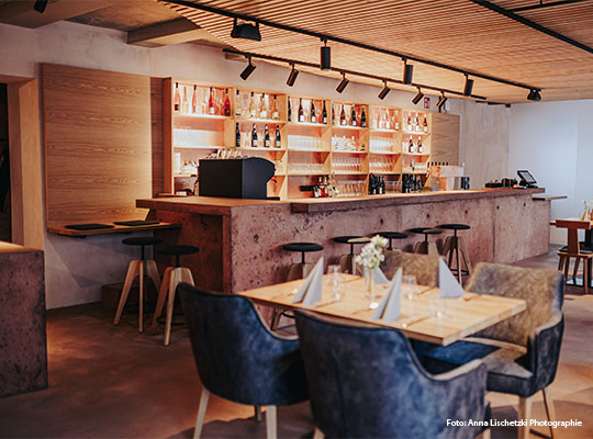 Innensicht mit Sicht auf Bar mit einem kleinem Tisch, an welchem vier Stühle stehen. Auf dem Tisch sind zusammengefaltete Servietten