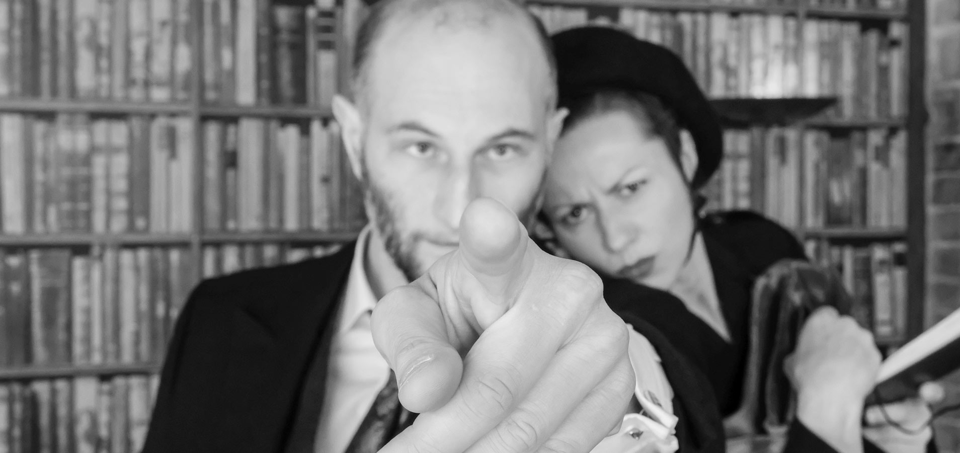 Mann zeigt mit dem Finger in die Kamera während sich eine Frau von rechts an ihn lehnt